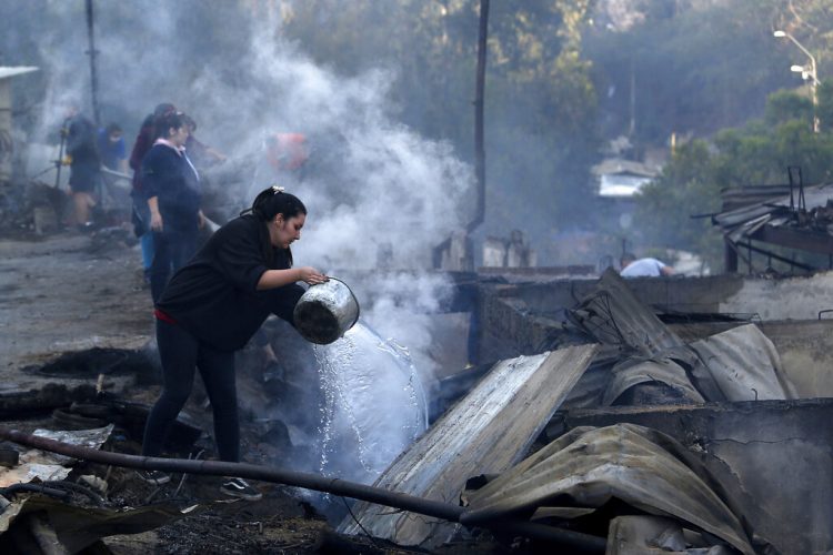 Residentes arrojan agua sobre los restos de sus casas el miércoles 25 de diciembre de 2019, después que un incendio dañó decenas de viviendas en las afueras de Valparaíso, Chile. Foto: Raul Zamora/Aton Chile vía AP.