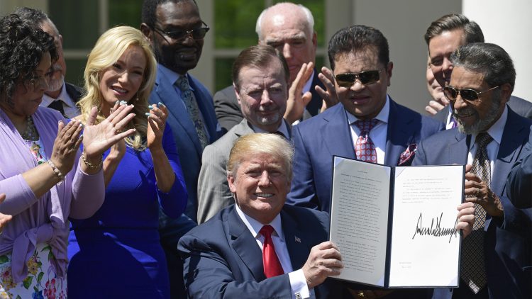 El pastor Guillermo Maldonado, en la foto de gafas oscuras a la izquierda y  en segundo plano, de Trump, participa en la ceremonia de la firma de una proclama presidencial el Día Nacional de la Oración, en mayo. (Foto AP/Susan Walsh