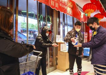 Un empleado distribuye desinfectante a clientes a la entrada de un supermercado en Wuhan, en la provincia de Hubei, en el centro de China, el sábado 25 de enero de 2020, debido a una epidemia de un mortal virus que fecta las vías respiratorias. (Chinatopix vía AP)