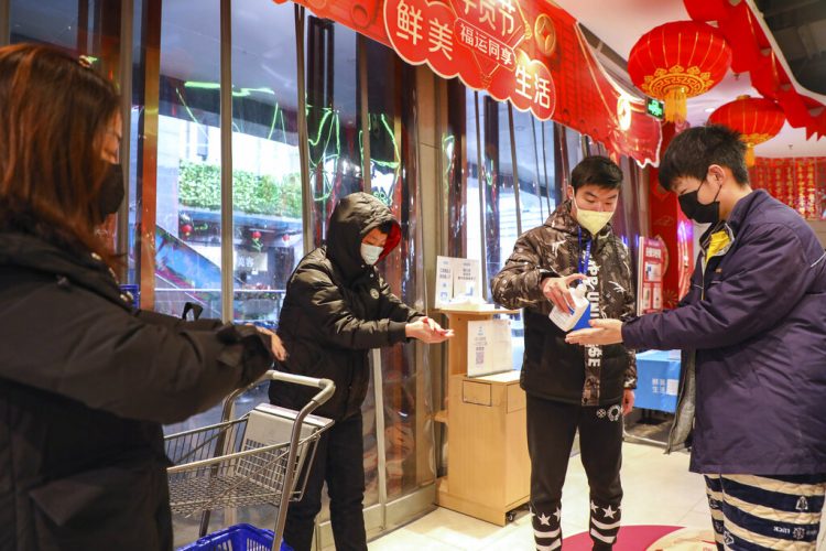 Un empleado distribuye desinfectante a clientes a la entrada de un supermercado en Wuhan, en la provincia de Hubei, en el centro de China, el sábado 25 de enero de 2020, debido a una epidemia de un mortal virus que fecta las vías respiratorias. (Chinatopix vía AP)