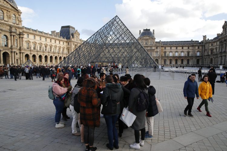 Turistas esperan y empleados en huelga se manifiestan en la entrada al Museo del Louvre, París, viernes 17 de enero de 2020. El museo estaba cerrado en medio de huelgas contra el plan del gobierno de reformar el sistema jubilatorio. (AP Foto/Francois Mori)