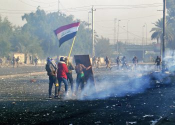 Manifestantes ondeando la bandera nacional mientras las fuerzas de seguridad lanzan gas lacrimógeo a una protesta en el centro de Bagdad, Irak, el lunes 20 de enero de 2020. Foto: AP/Hadi Mizban