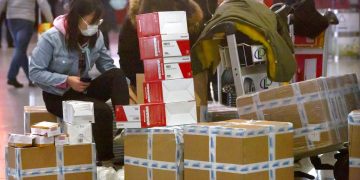 Una viajera sentada junto a cajas de mascarillas para la cara y respiradores en el aeropuerto internacional de Beijing, el 30 de enero de 2020. Foto: Mark Schiefelbein / AP.