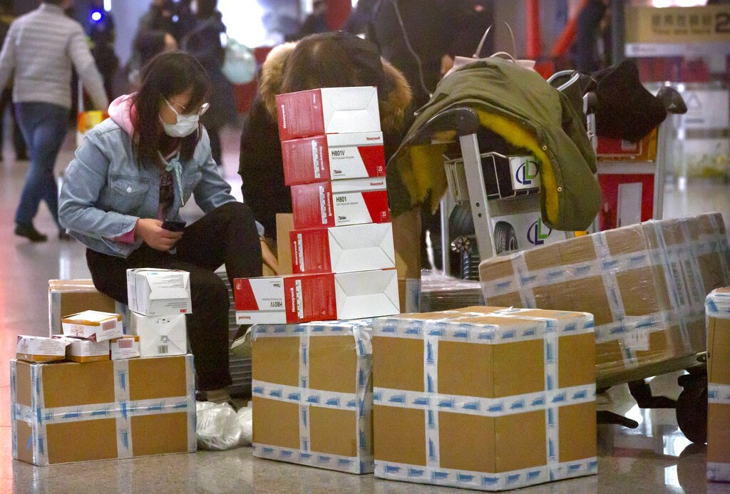 Una viajera sentada junto a cajas de mascarillas para la cara y respiradores en el aeropuerto internacional de Beijing, el 30 de enero de 2020. Foto: Mark Schiefelbein / AP.