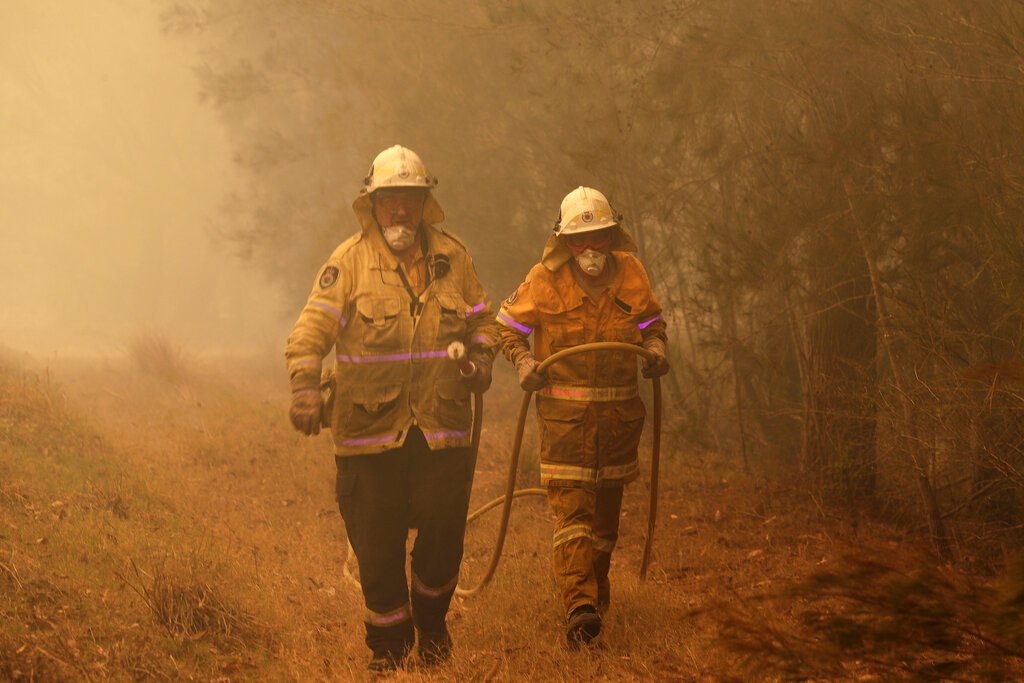 Dos bomberos arrastran una manguera de agua tras apagar un incendio cerca de Moruya, Australia, el 4 de enero de 2020. Foto: Rick Rycroft / AP.