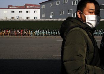Un hombre con mascarilla junto a una fila de bicicletas de alquiler estacionadas ante una estación de metro en Beijing, el lunes 10 de febrero de 2020. (AP Foto/Andy Wong)