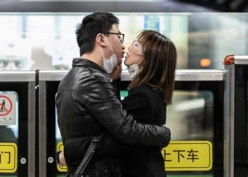 Una pareja se quita las mascarillas de seguridad y se besa mientras espera el transporte público en Shanghái, China. Foto: Liu Xingzhe / EFE: