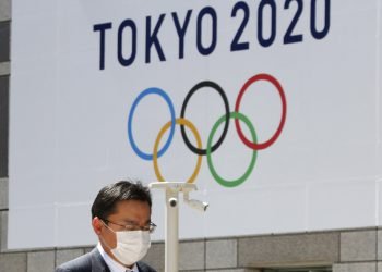 Un hombre con una mascarilla pasa junto a un cartel que anuncia los Juegos Olímpicos de Tokio del 2020, ya pospuestos para el próximo año. Foto: Koji Sasahara / AP / Archivo.