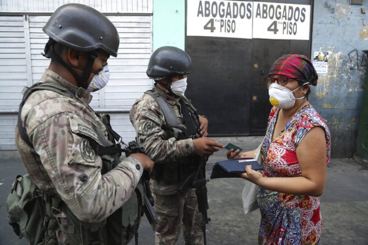 Una mujer explica a los soldados que está buscando alcohol en farmacias, antes de que la dejen continuar su camino, en el tercer día del estado de emergencia en Lima, Perú, el miércoles 18 de marzo de 2020. Foto: Martín Mejia/AP.