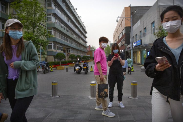 Varias personas cubren sus caras con máscaras como medida contra la propagación del nuevo coronavirus mientras caminan al aire libre por una zona comercial en Beijing, el viernes 24 de abril de 2020.  (AP Foto/Mark Schiefelbein)