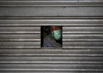 Un hombre con una mascarilla se asoma por una pequeña apertura en la puerta de una farmacia en espera de clientes en Igualada, España. Foto: Felipe Dana/AP.