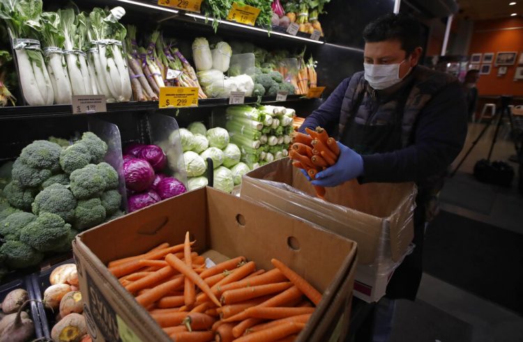 Un empeado luciendo una máscara protectora y guantes contra el COVID-19, coloca zanahorias en los estantes en el Gus's Community Market el viernes, 27 de marzo del 2020, en San Francisco.  (AP Foto/Ben Margot)