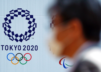 Un hombre con una mascarilla protectora contra infecciones respiratorias como la COVID-19 pasa junto al logo de los juegos olímpicos Tokio 2020. Foto: Eugene Hoshiko / AP / Archivo.