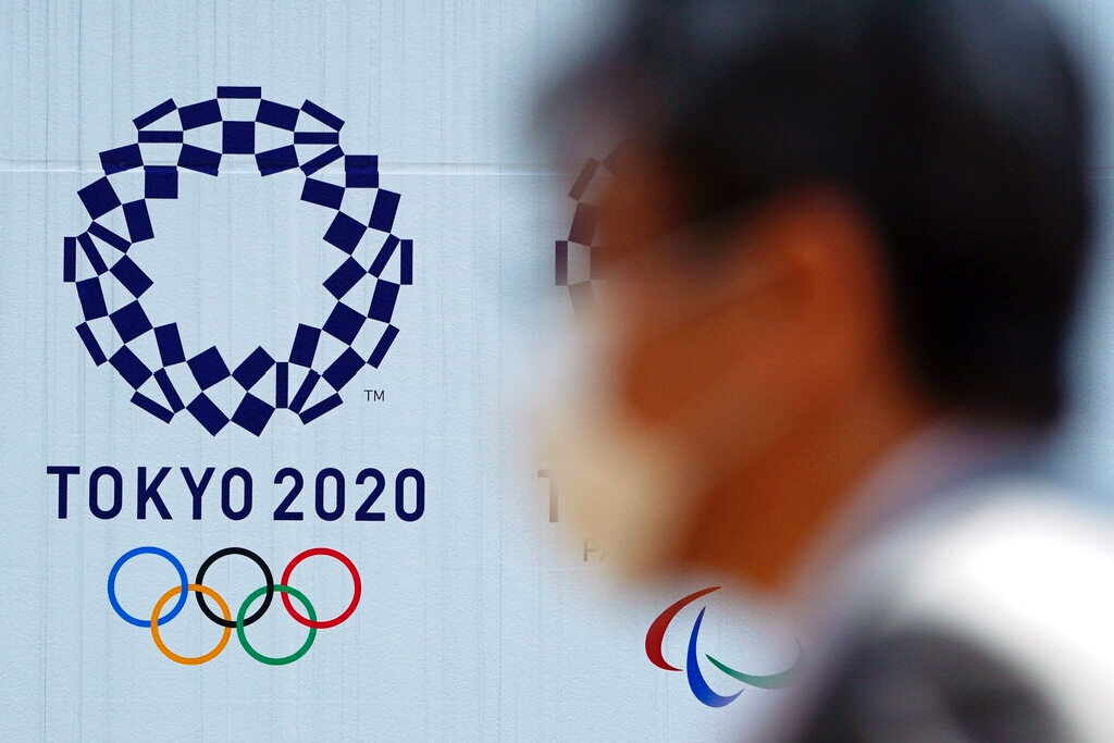 Un hombre con una mascarilla protectora contra infecciones respiratorias como la COVID-19 pasa junto al logo de los juegos olímpicos Tokio 2020. Foto: Eugene Hoshiko / AP / Archivo.