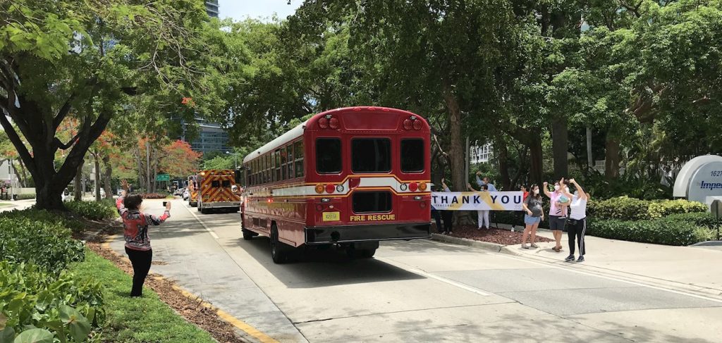 Personas aplauden a unos camiones de bomberos que desfilan haciendo sonar sus sirenas y luces por las calles de Miami, Florida, como una muestra de agradecimiento por su labor durante la pandemia de la Covid-19, el 20 de mayo de 2020. Foto: Ana Mengotti / EFE.