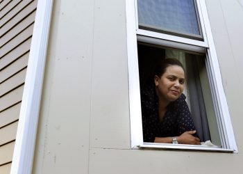 En imagen del miércoles 20 de mayo de 2020, Wendy De Los Santos, originaria de la República Dominicana, posa para una fotografía desde una ventana de su hogar, en Malden, Massachusetts. (AP Foto/Steven Senne)