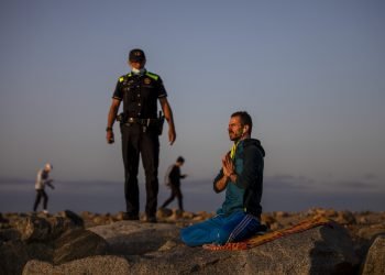 Un agente de policía habla con un hombre en una playa reabierta para actividades deportivas en Barcelona. Foto: Emilio Morenatti/AP