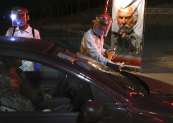 Trabajadores con trajes protectores desinfectan autos que entran a un autocine situado junto a la torre Milad, en Teherán, el viernes 1 de mayo del 2020. Irán es el epicentro de la pandemia del Covid-19 en la región. Foto: AP/Vahid Salemi.