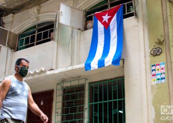 Un hombre pasa cerca de una bandera cubana colgada en una calle de La Habana, el 1 de mayo de 2020. Foto: Otmaro Rodríguez / Archivo.