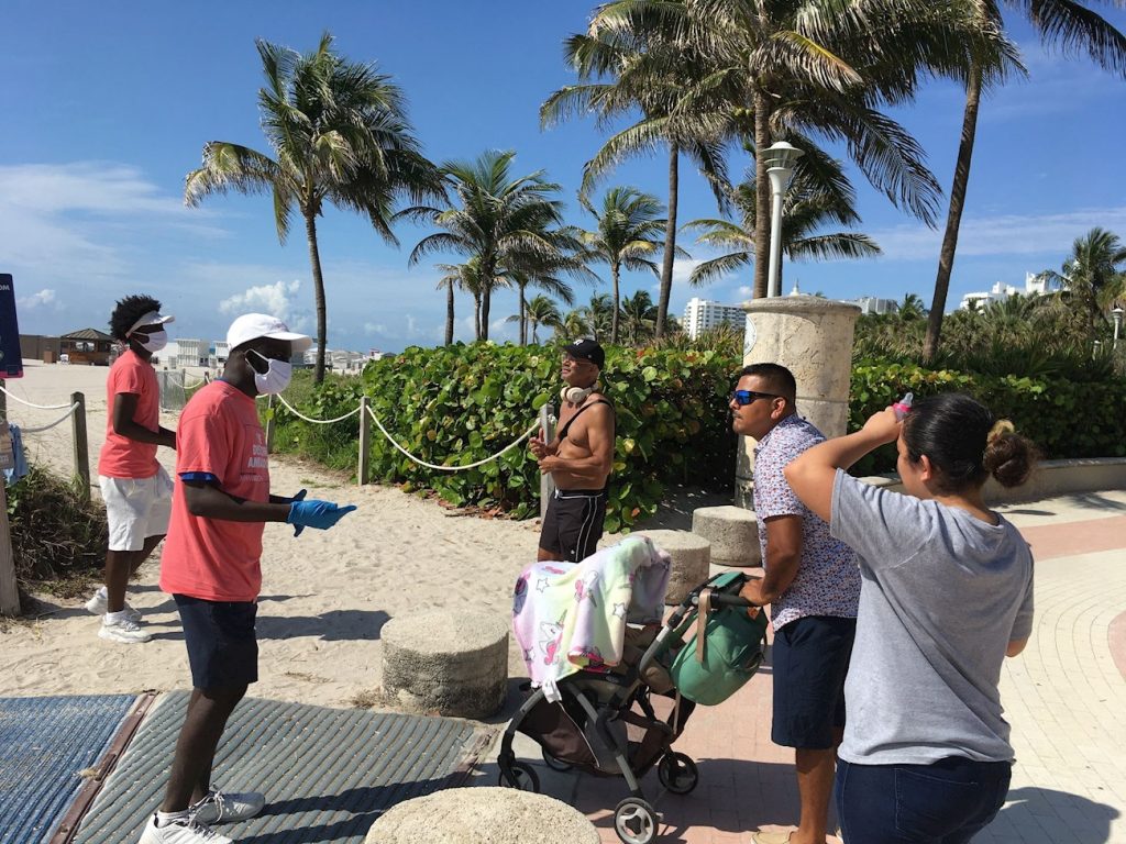 Unos jóvenes revisan las máscaras de unas personas a su llegada a la playa de Miami Beach, Florida, el 10 de junio de 2020. Foto: Ivonne Malaver / EFE.