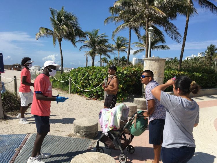 Unos jóvenes revisan las máscaras de unas personas a su llegada a la playa de Miami Beach, Florida, el 10 de junio de 2020. Foto: Ivonne Malaver / EFE.