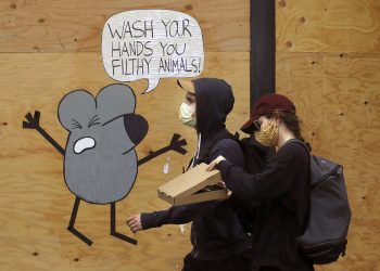 Un hombre y una mujer con mascarillas pasan junto a un mural que recuerda a la gente que se lave las manos, en una tienda protegida por tablones en San Francisco.  Foto: Jeff Chiu / AP