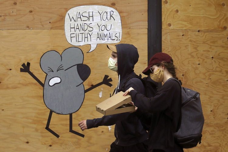 Un hombre y una mujer con mascarillas pasan junto a un mural que recuerda a la gente que se lave las manos, en una tienda protegida por tablones en San Francisco.  Foto: Jeff Chiu / AP