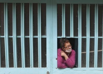 Una mujer observa desde la ventana de su casa mientras espera recibir comida gratis del gobierno de la ciudad el viernes 12 de junio de 2020, en Bogotá, Colombia, donde continúan las medidas de prevención por el coronavirus. (AP Foto/Fernando Vergara)