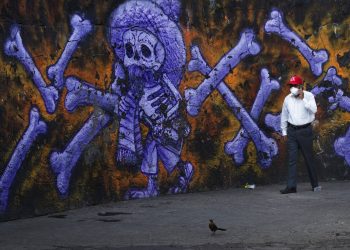 El responsable de varios cementerios públicos camina ante un mural de un esqueleto y huesos en el exterior del Panteón San Nicolás Tolentino, Iztapalapa, Ciudad de México. Foto: Marco Ugarte/AP.