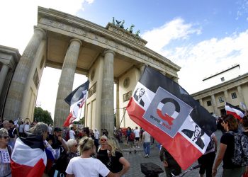 Personas con banderas con la cara del presidente estadounidense Donald Trump asisten a una manifestación contra las restricciones por la pandemia frente a la Puerta de Brandenburgo en Berlín, Alemania, el sábado 29 de agosto de 2020. (AP Foto/Michael Sohn)