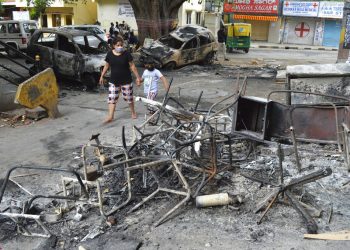 Una mujer y un niño pasan junto a los restos de vehículos y muebles quemados en las protestas de Bengaluru, India, el miércoles 12 de agosto de 2020. Al menos tres personas murieron en la ciudad en choques entre la policía y manifestantes que protestaban por una publicación de Facebook que consideraban como una ofensa al islam. Foto: AP.