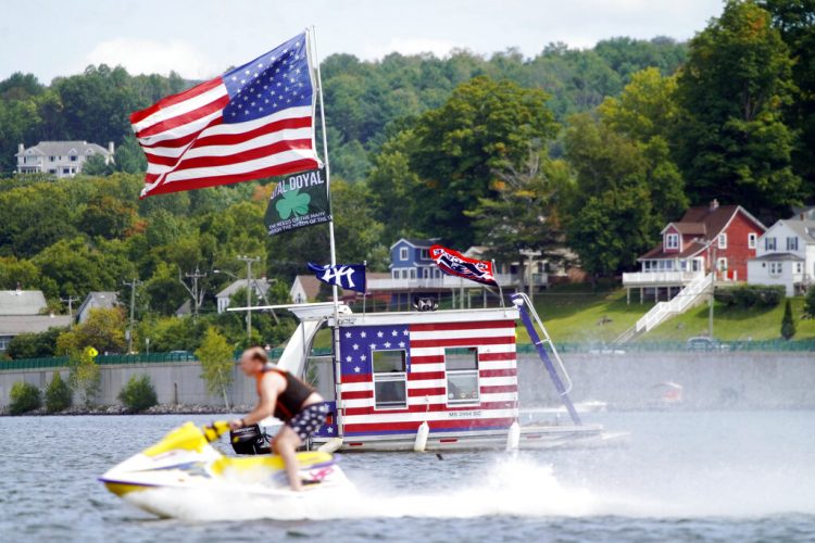 Una persona pasa con su moto acuática frente a un bote adornado con banderas estadounidenses en Pittsfield, Massachusetts, el lunes 7 de septiembre de 2020. Foto: Ben Garver/The Berkshire Eagle vía AP.