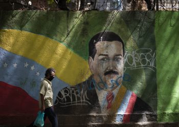 Un individuo con mascarilla pasa frente a un mural del presidente Nicolás Maduro en Caracas el 22 de julio de 2020. Foto: Ariana Cubillos/AP.