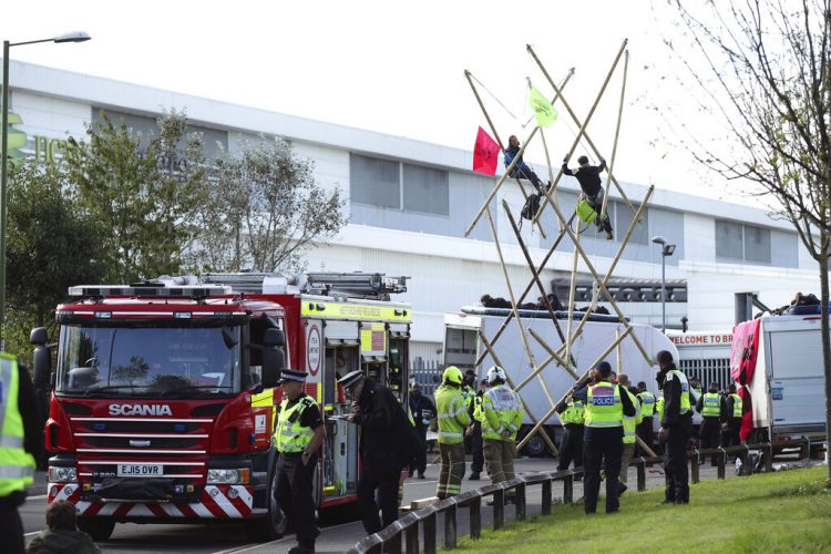 Policías y bomberos movilizados ante una imprenta de Broxbourne, donde varios manifestantes bloquean la carretera con una estructura, en Broxbourne, Hertfordshire, Inglaterra, el sábado 5 de septiembre de 2020. Foto: Yui Mok/PA via AP.
