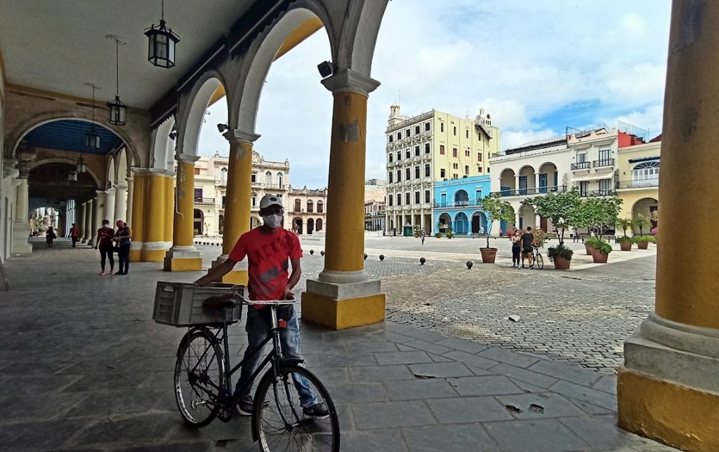Un hombre con nasobuco camina con su bicicleta por los portales de una plaza en la Habana Vieja. Foto: Ernesto Mastrascusa / EFE.