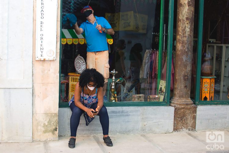 Una mujer revisa su teléfono móvil en las afueras de una tienda que se prepara para su reapertura, tras la flexibilización de las restricciones por la COVID-19 en La Habana. Foto: Otmaro Rodríguez.