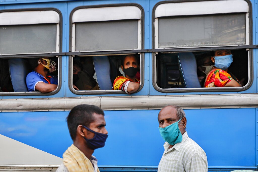 Pasajeros, con mascarilla para protegerse del coronavirus, esperan en el interior de un autobús mientras dos peatones cruzan por delante, en una estación de buses en Calcuta, India, el 1 de octubre de 2020. Foto: AP Foto/Bikas Das.