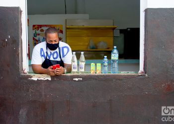 Un dependiente con mascarilla revisa su teléfono móvil tras la flexibilización de las restricciones por la COVID-19 en La Habana. Foto: Otmaro Rodríguez.