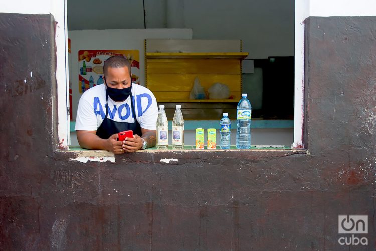Un dependiente con mascarilla revisa su teléfono móvil tras la flexibilización de las restricciones por la COVID-19 en La Habana. Foto: Otmaro Rodríguez.