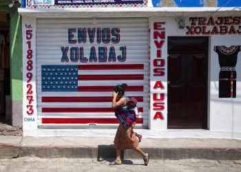 Una mujer con un niño pasa junto a un negocio de mensajería en el pueblo mayoritariamente indígena de Joyabaj, Guatemala. La mitad de lsus residentes dependen de las remesas. Foto: Moises Castillo/AP.