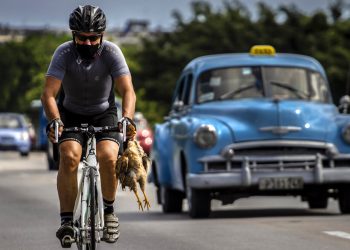 Un ciclista con máscara como medida de precaución contra la propagación del nuevo coronavirus lleva un pollo en la mano mientras pedalea su bicicleta en La Habana, Cuba, el domingo 11 de octubre de 2020. Foto: Ramón Espinosa/AP.