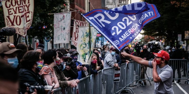 Un seguidor del presidente Trump ondea una bandera frente a un grupo de seguidores de Joe Biden en el exterior de un centro de escrutinio electoral en Filadelfia. Foto: Mario Cruz / EFE