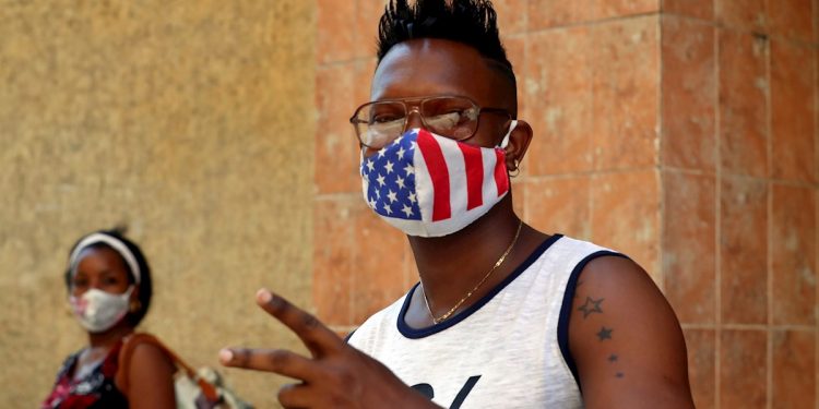 Un joven usa una mascarilla con diseño de la bandera de Estados Unidos, mientras posa para una foto en La Habana. Foto: Ernesto Mastrascusa / EFE.