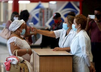 Trabajadoras del aeropuerto de La Habana toman la temperatura a una viajera tras el reinicio de las operaciones regulares, suspendidas desde hace meses a causa de la pandemia. Foto: Yander Zamora / EFE.
