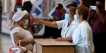 Trabajadoras del aeropuerto de La Habana toman la temperatura a una viajera tras el reinicio de las operaciones regulares, suspendidas desde hace meses a causa de la pandemia. Foto: Yander Zamora / EFE.