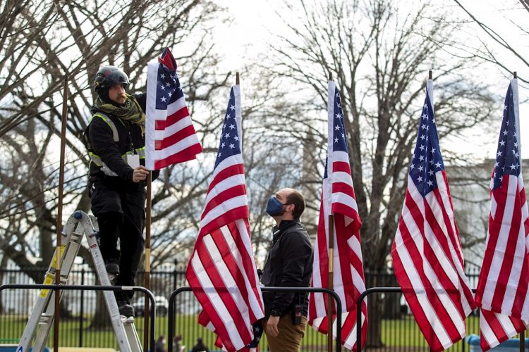 Dos trabajadores colocan banderas estadounidenses en mástiles en preparación para la inauguración en el Capitolio, el miércoles. | SHAWN THEW/EFE