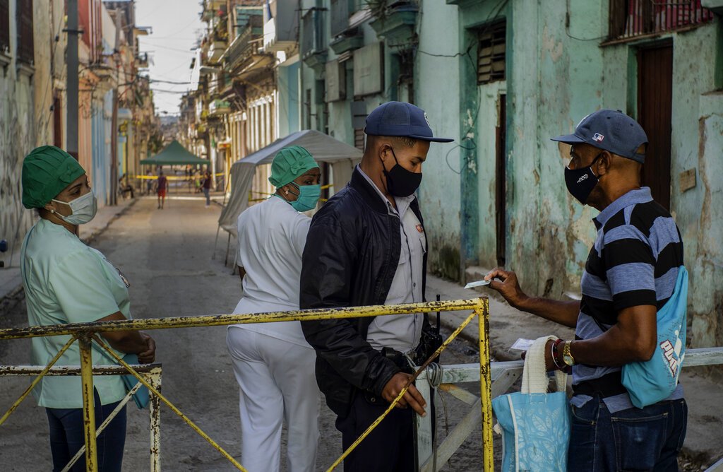 Un residente muestra su identificación a un oficial de policía que está limitando el acceso a un vecindario como una forma de frenar la propagación de la pandemia de COVID-19, mientras enfermeras están detrás en La Habana, Cuba, el lunes 22 de febrero de 2021. Foto: AP/Ramon Espinosa.