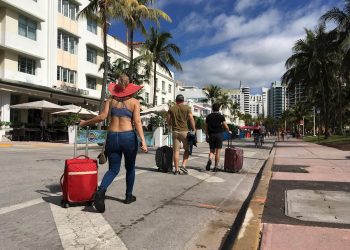 Varias personas caminan con su equipaje a través de la avenida Ocean Drive, en Miami Beach, Florida, luego de decretarse el toque de queda nocturno por sus autoridades. Foto: Ivonne Malaver / EFE.