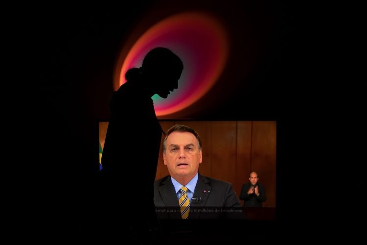 Una mujer grita "fuera Bolsonaro" mientras el presidente brasileño Jair Bolsonaro ofrece un discurso televisado, en Brasilia (Brasil). Foto: Joédson Alves / EFE. Tomada de El País (Brasil).
