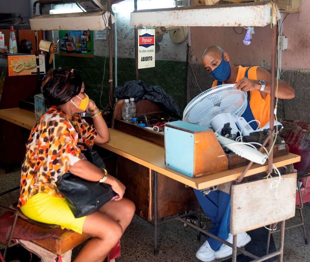 Una mujer espera que un mecánico le repare un ventilador, en un taller de equipos electrodomésticos en La Habana. Foto: Yander Zamora / EFE.